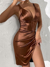 Close-up of a woman's torso in a brown satin dress with a plunging neckline and high slit, against a textured wall.