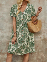 Woman wearing a green and white floral print button-down midi dress with short sleeves and a V-neck, holding a straw handbag.