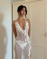 Woman in a sheer white floral applique dress, posing with hands behind her back.