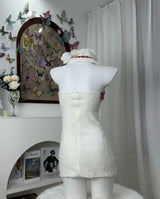 Back view of a white strapless dress with red plaid trim and red ribbon accents, displayed on a mannequin.