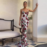 Woman wearing a floor-length floral print dress with spaghetti straps and a halter neckline, leaning against a pillar outdoors with a bench and checkered floor.