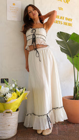 Woman posing in a white crinkle fabric two-piece set with black trim and tie details.