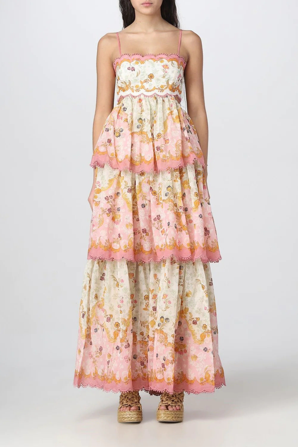 Full-body view of a woman wearing a tiered floral print maxi dress with pink pom-pom trim and a sweetheart neckline.