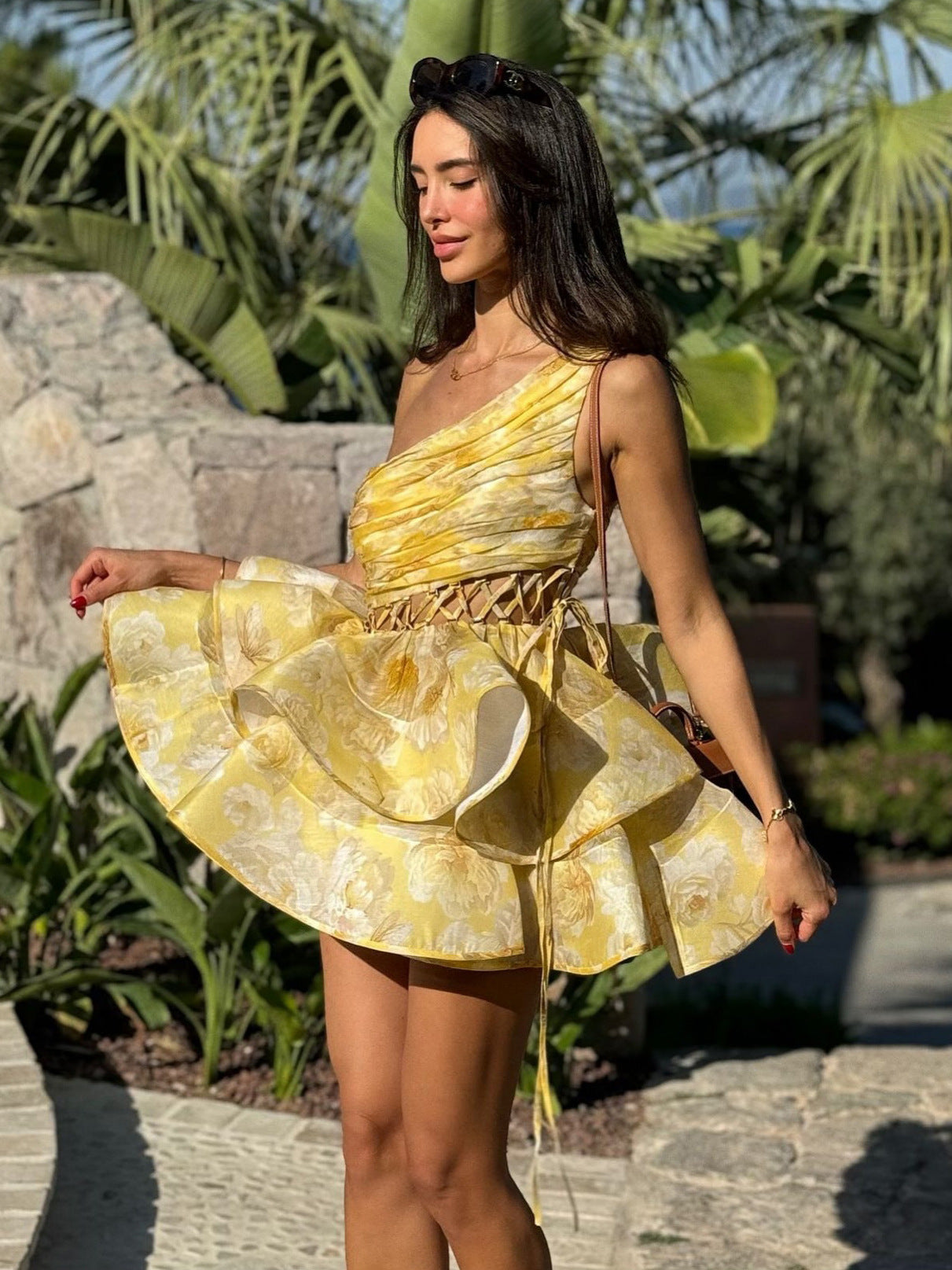 Woman wearing a yellow floral print one-shoulder mini dress with a ruffled skirt posing outdoors.