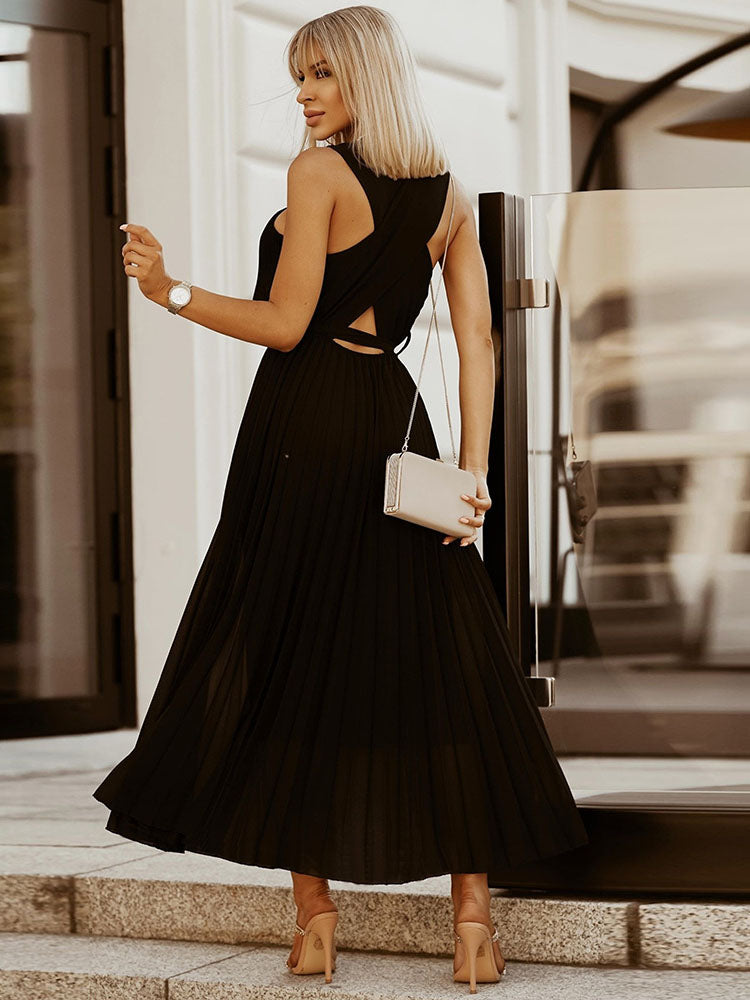 Back view of a woman in a black pleated maxi dress with a cut-out detail at the waist.