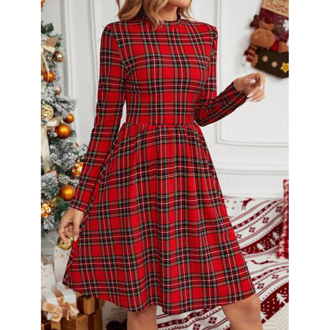 Detail view of a woman's torso in a red plaid long-sleeve fit and flare dress with a round neck, against a backdrop of a Christmas tree and decorations.