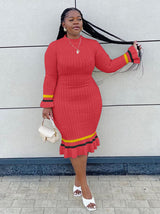 Woman in a red ribbed knit midi dress with long sleeves and striped details, posing with her hair.
