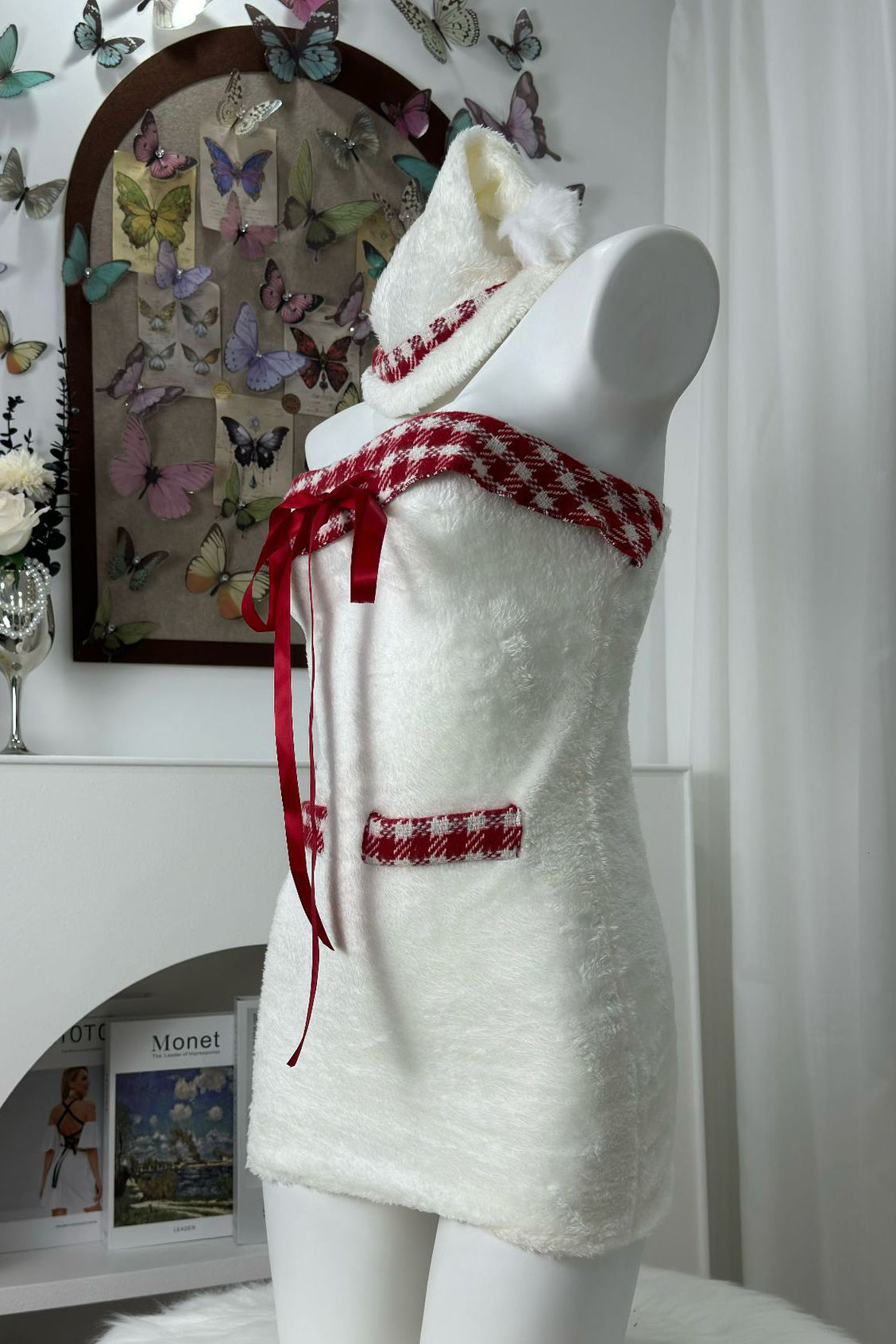 Side profile of a white strapless dress with red plaid trim and red ribbon accents, displayed on a mannequin.
