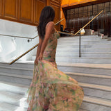 Woman in a floral print maxi dress with a high slit and corset bodice turning away on marble stairs.