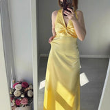 Woman taking a mirror selfie in a yellow satin maxi dress with a twisted V-neckline and halter straps.