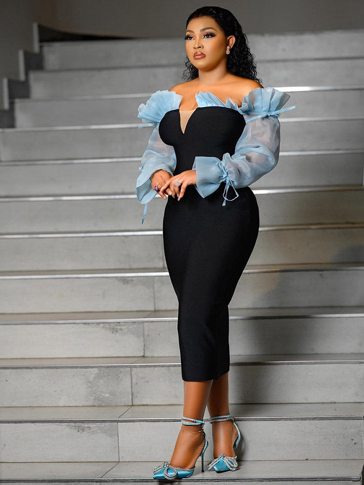 Full body shot of a woman in a black fitted dress with blue sheer sleeves on a staircase