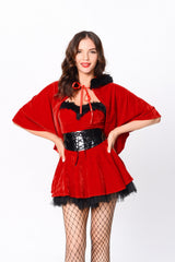 Woman wearing a red velvet costume with a cape, corset belt, and fishnet stockings, posing with hands on hips.