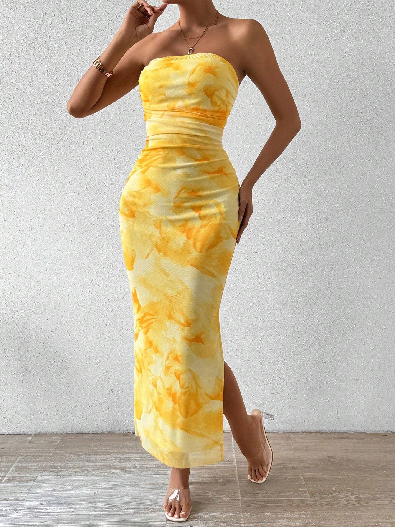 A woman poses in a yellow tie-dye print strapless maxi dress, touching her hair.