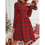 Close-up of a woman in a red plaid long-sleeve fit and flare dress with a round neck, posing in a festive setting.