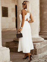 Side view of a woman in a white pleated maxi dress with a cut-out detail and high heels.