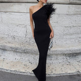 Full-length view of a woman in a black one-shoulder fitted gown with feather shoulder embellishment, holding a silver clutch.