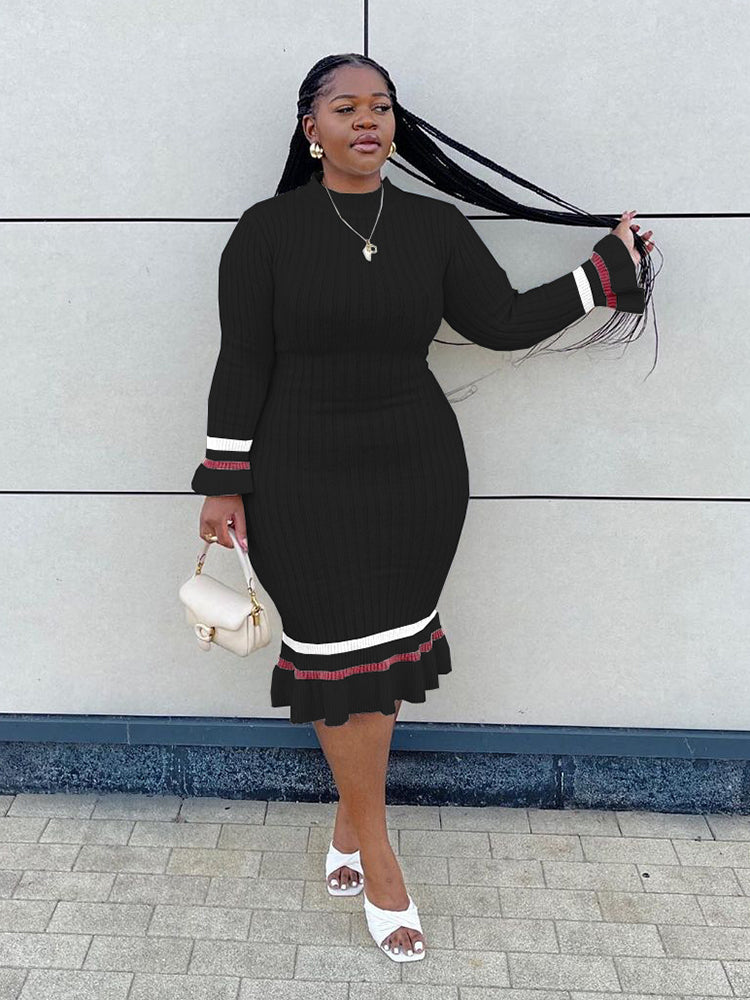 Woman in a black ribbed knit midi dress with long sleeves and striped details, posing with her hair.