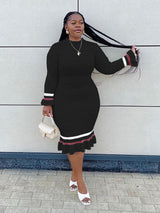 Woman in a black ribbed knit midi dress with long sleeves and striped details, posing with her hair.