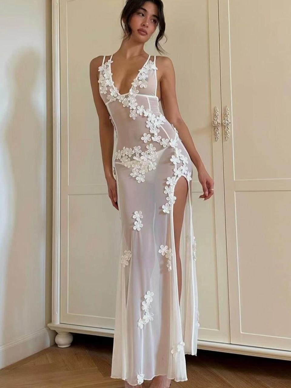 Woman wearing a long, sheer white dress with floral appliques and a high slit.