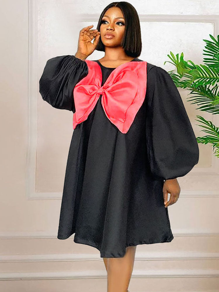 Close-up of the pink bow on the black dress, showing the satin-like fabric and pleating.