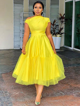 woman wearing a bright yellow fit and flare dress with an asymmetrical neckline and a tiered tulle skirt
