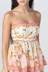 Close-up of a woman wearing a floral print maxi dress with pink scalloped and pom-pom trim.