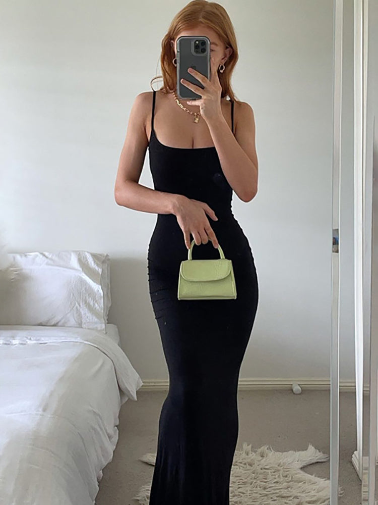 Woman in a black maxi dress holding a small green handbag, taking a mirror selfie