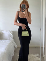 Woman in a black maxi dress holding a small green handbag, taking a mirror selfie