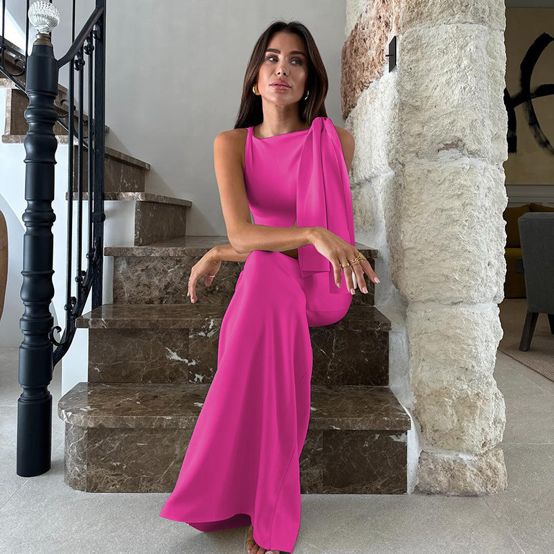 Woman in a bright pink floor-length dress with an asymmetrical neckline and draped shoulder detail, sitting on a marble staircase.