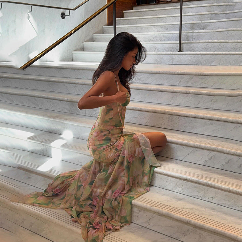 Woman in a floral print maxi dress with a high slit and corset bodice sitting on marble stairs.