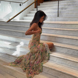 Woman in a floral print maxi dress with a high slit and corset bodice sitting on marble stairs.