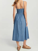 back view of a woman in a blue denim midi dress with spaghetti straps