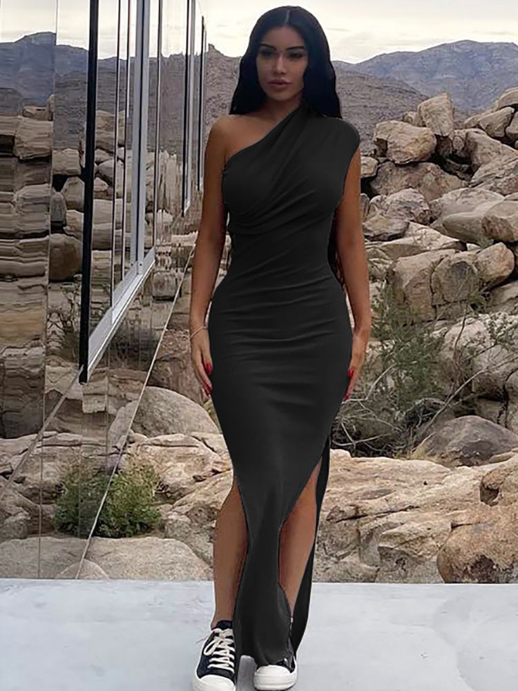 Woman wearing a black one-shoulder ruched maxi dress with a high slit and sneakers, standing outdoors with a rocky, mountainous background.