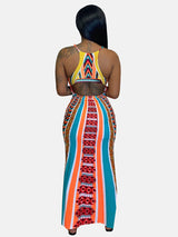 Back view of a woman wearing a colorful geometric print maxi dress with spaghetti straps and a side slit.