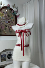 Side view of a white strapless dress with red plaid trim and red ribbon accents, displayed on a mannequin with a matching hat.