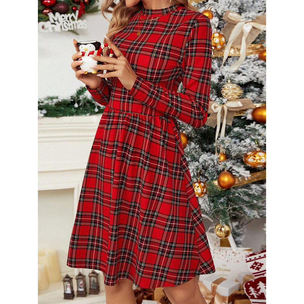Woman holding a small figurine while wearing a red plaid long-sleeve fit and flare dress with a round neck, with a Christmas tree in the background.