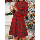 Woman holding a small figurine while wearing a red plaid long-sleeve fit and flare dress with a round neck, with a Christmas tree in the background.