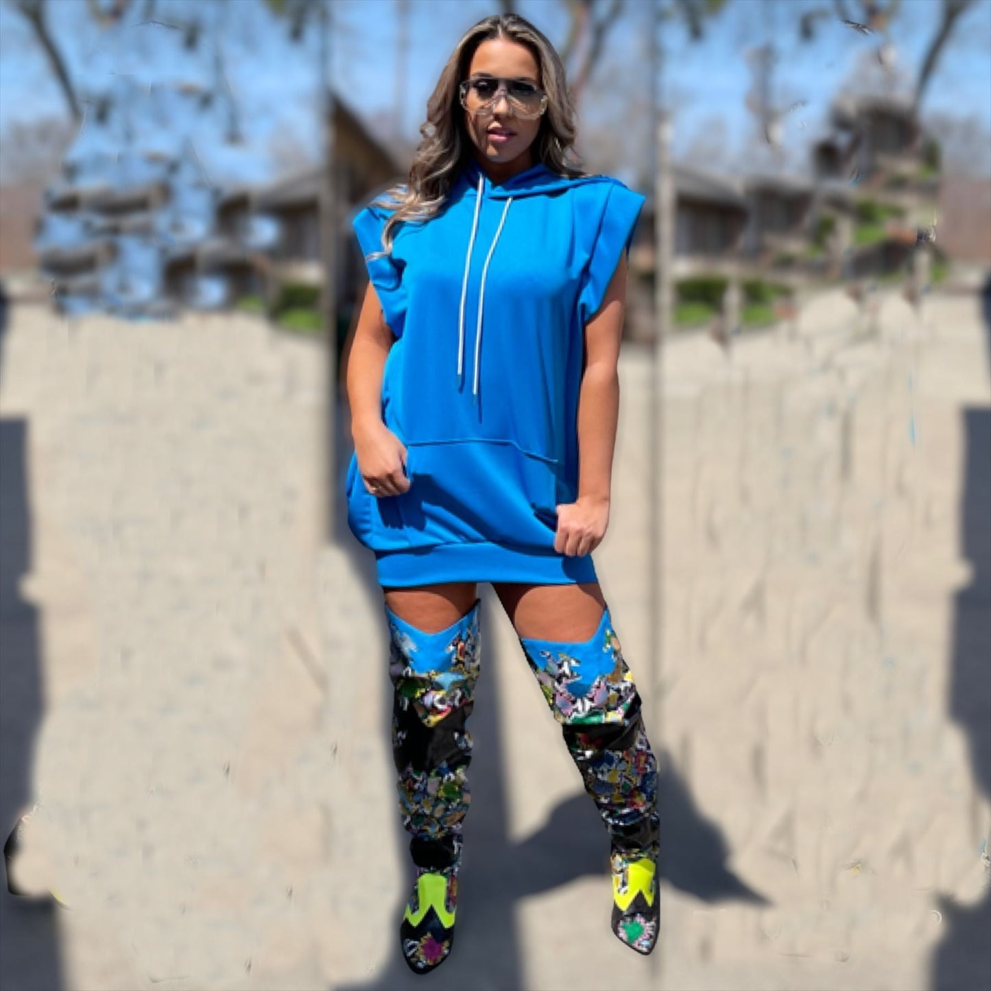 Woman wearing a bright blue sleeveless hooded mini dress with white drawstrings and colorful thigh-high boots.