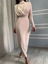 A woman wearing a pale pink long-sleeved draped neck sheath dress.