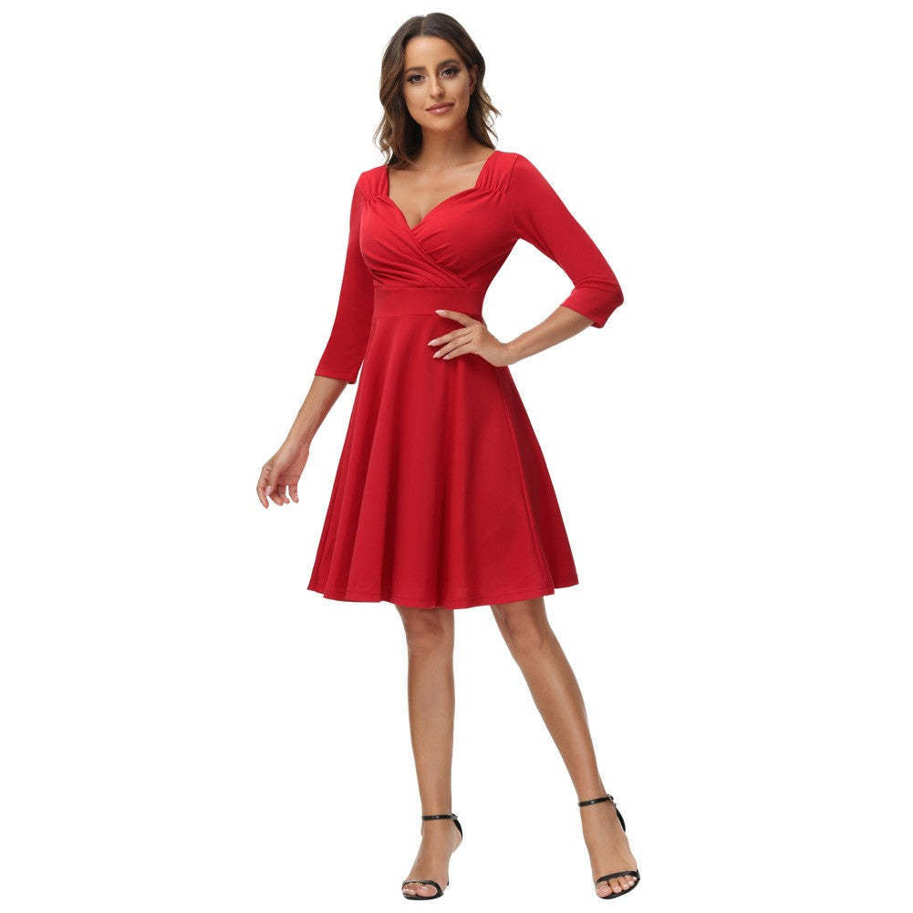 Woman in a red fit and flare dress with a surplice neckline and three-quarter sleeves, posing with one hand on her hip.