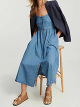woman sitting on a stool wearing a blue denim midi dress and a blazer draped over her shoulders, showing the front of the dress