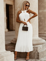 Woman wearing a white pleated maxi dress with a halter neckline and a mini handbag.