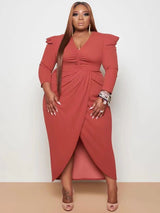 Woman wearing a rust ruched V-neck sheath dress with an asymmetrical tulip hem and puffed shoulders.