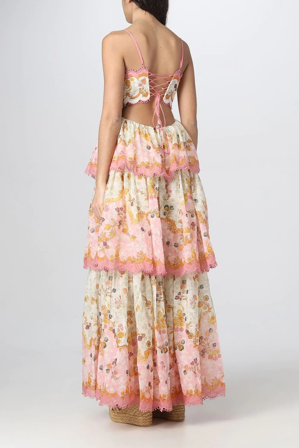 Back view of a woman in a floral print maxi dress, showing the lace-up back detail and tiered skirt.