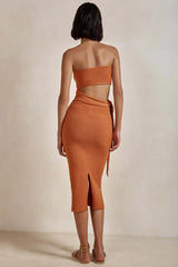Woman wearing an orange strapless knit crop top and matching midi skirt with a tie waist and side slit, shown from the back.