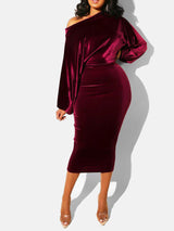 Woman wearing a burgundy velvet off-the-shoulder midi dress with long sleeves and clear heels, posing against a white background.