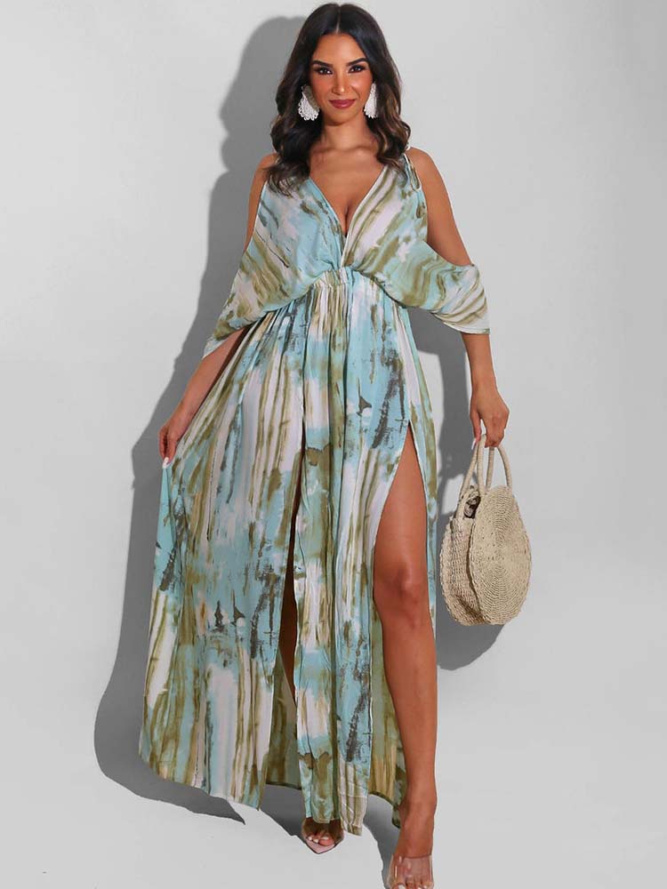 Woman wearing a long, flowing maxi dress with a tie-dye print and high slits, holding a straw bag.