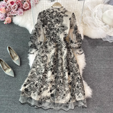 Close-up of the bodice of a black and white floral embroidered midi dress, highlighting the sheer fabric, sequins, and mock neckline.