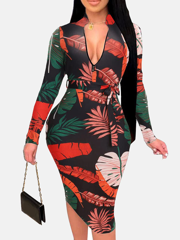 Woman in a black midi dress with a red and green leaf print, V-neck, long sleeves, and a belted waist.