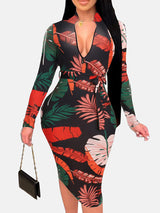 Woman in a black midi dress with a red and green leaf print, V-neck, long sleeves, and a belted waist.